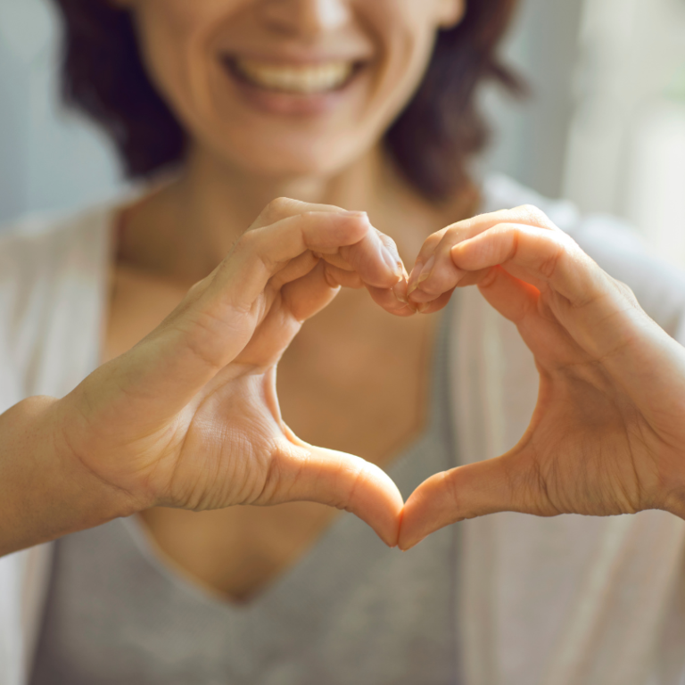Smiling woman holding her hands out in the shape of a heart.